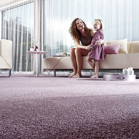 Frau mit Kind sitzt lachend auf Sofa im modernen Wohnzimmer mit flauschigem Teppichboden.