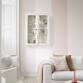 Helles Wohnzimmer mit pastellrosa Wänden, gemütlichem Sofa und dekorativem Wandregal.