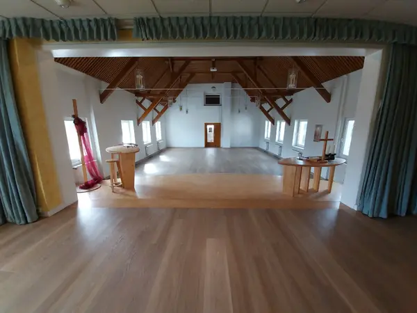 Heller Kirchenraum mit Holzbalken, Bühne, Kreuz und Fenstern im Saal