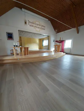 Kircheninnenraum mit Altar, Kreuz und Kanzel unter Holzdecke, helles Licht