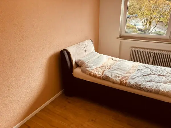 Schlafzimmer mit Bett, Fensterblick ins Grüne und Heizkörper unter dem Fenster