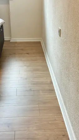 Leere Zimmerecke mit Laminatboden in Holzoptik und weißer Sockelleiste