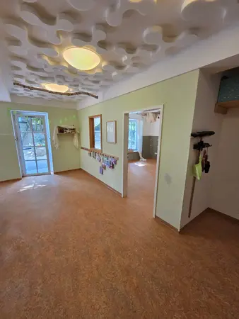 Heller Gruppenraum mit Puzzle-Deckenpaneelen, Türfenster und Korkboden