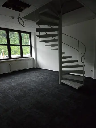 Leerer Büroraum mit Wendeltreppe, großen Fenstern und Blick ins Grüne
