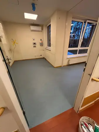 Leerer Klinikraum mit Vinylboden, Fenster, Heizkörper und Wandtechnikpanel