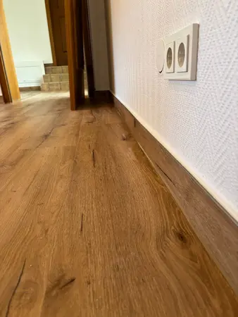 Steckdose an Wand über Holzfußboden im Flur, Nahaufnahme Innenraum