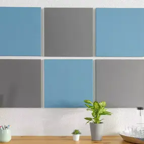 Sechs Akustikpaneele in Blau und Grau hängen modern dekoriert über einem Holzschreibtisch.