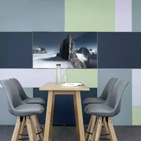 Moderner Konferenzraum mit Holztisch, vier grauen Stühlen und bunter Akustikwand.